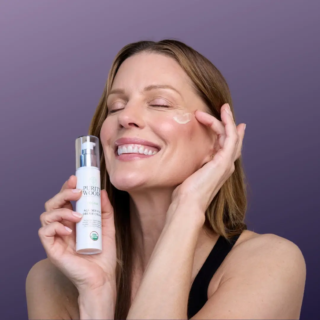 woman holding bottle of dream cream while applying cream to cheek and smiling