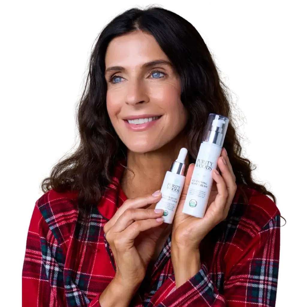 Person in a red plaid shirt smiles while holding two Purity Woods skincare products—Dream Cream and Hyper-Lift Serum—against a black background with white floral illustrations.