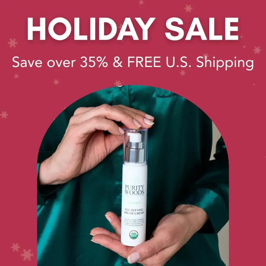 A person wearing a green satin garment holds a bottle of Purity Woods Organic Age-Defying Dream Cream, which displays the USDA Organic seal. The festive red background features snowflake graphics, and white promotional text at the top reads: "HOLIDAY SALE – Save over 35% & FREE U.S. Shipping," highlighting a seasonal skincare offer.