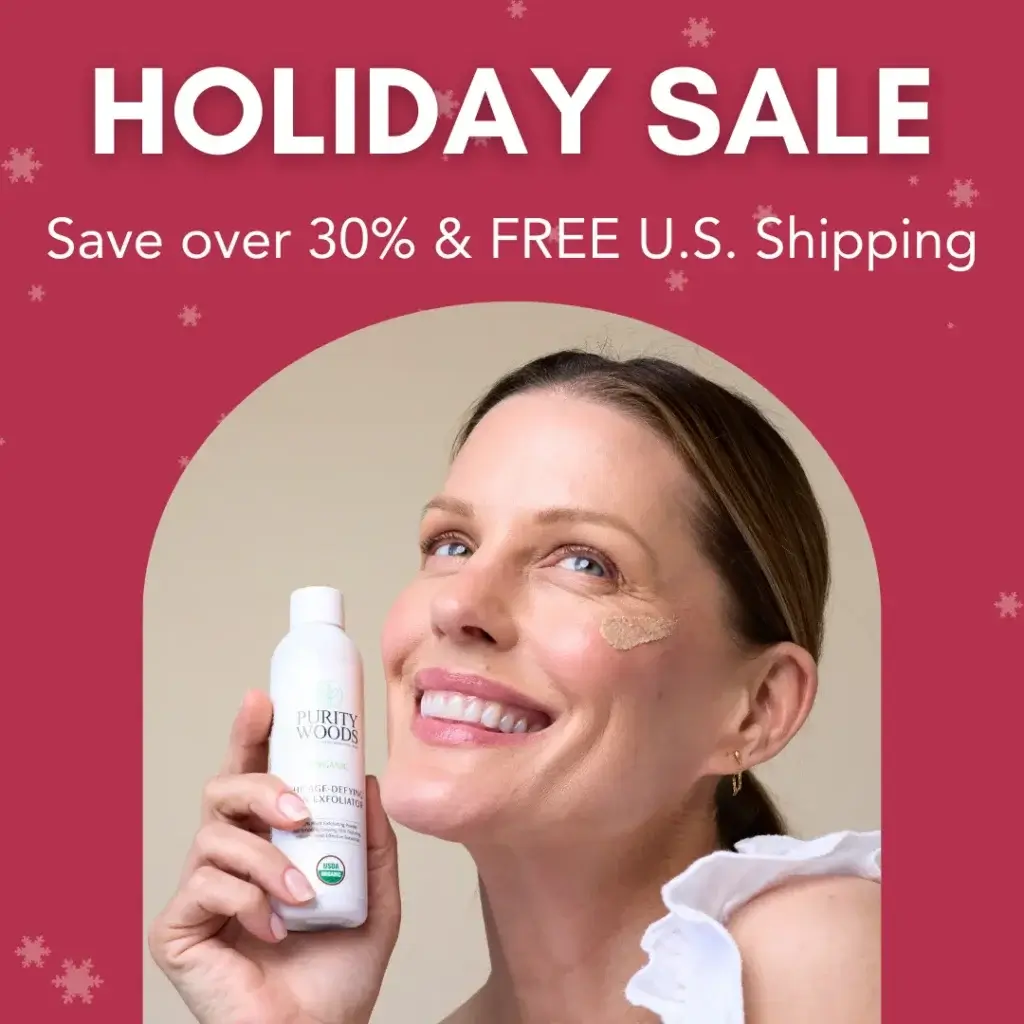 Alt text: A smiling person holds a bottle of Purity Woods skincare product labeled "Age-Defying Exfoliator" with a small amount applied to their cheek. The background is red with snowflake graphics, creating a festive holiday theme. Promotional text at the top reads: "HOLIDAY SALE – Save over 30% & FREE U.S. Shipping," highlighting a seasonal skincare offer.